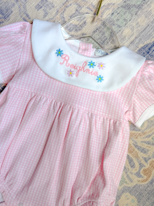 Pink checkered dress with embroidered name on a hanger against a patterned background