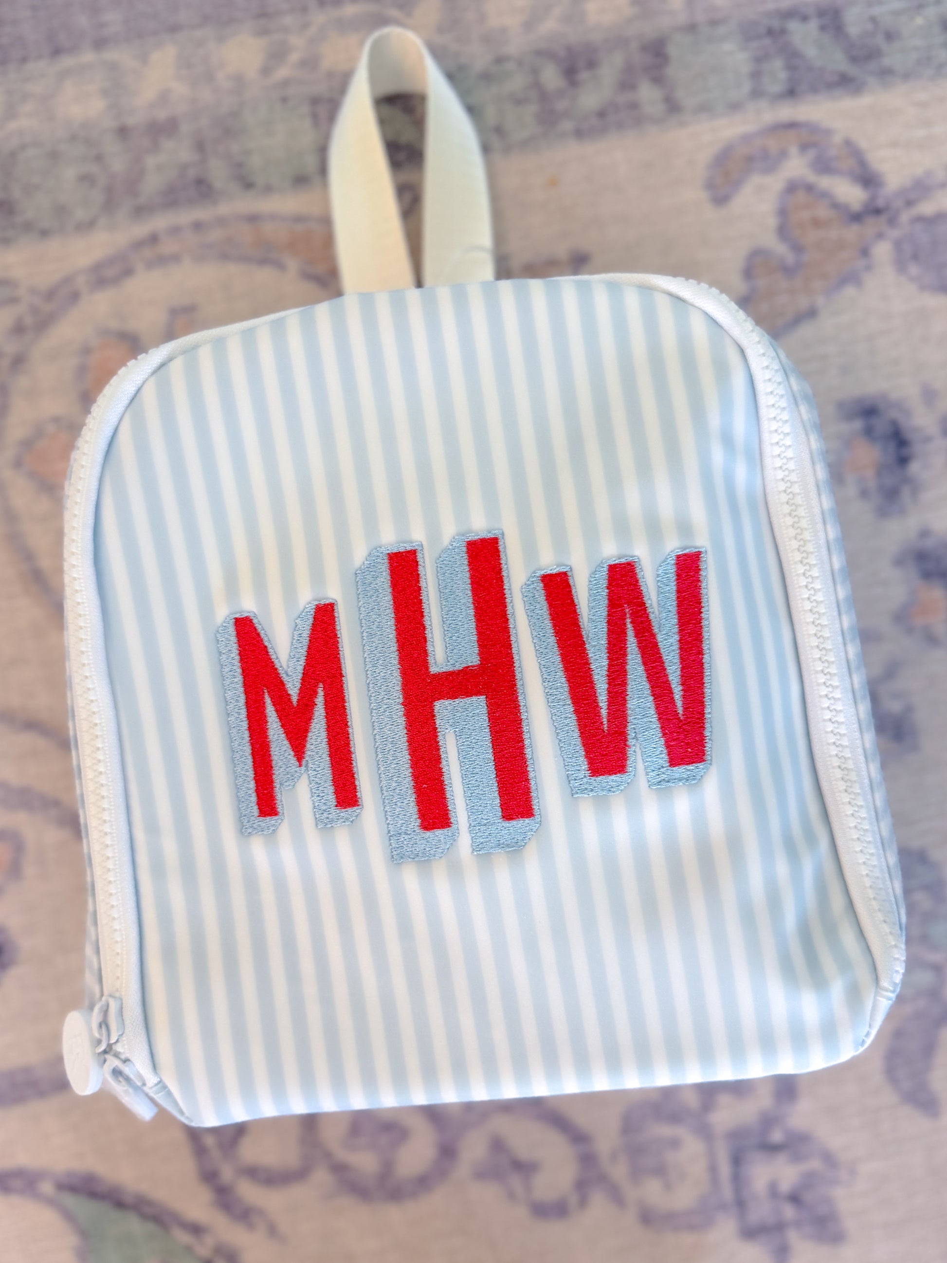 Small striped pouch with red letters 'MHW' on a patterned surface