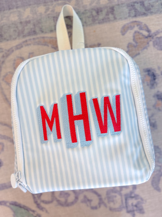 Small striped pouch with red letters 'MHW' on a patterned surface