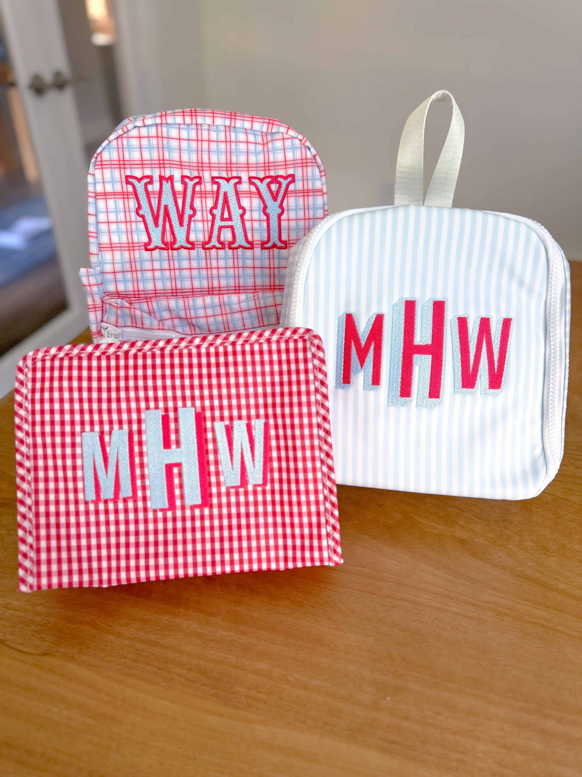 Three fabric pouches with monogrammed initials on a wooden surface.