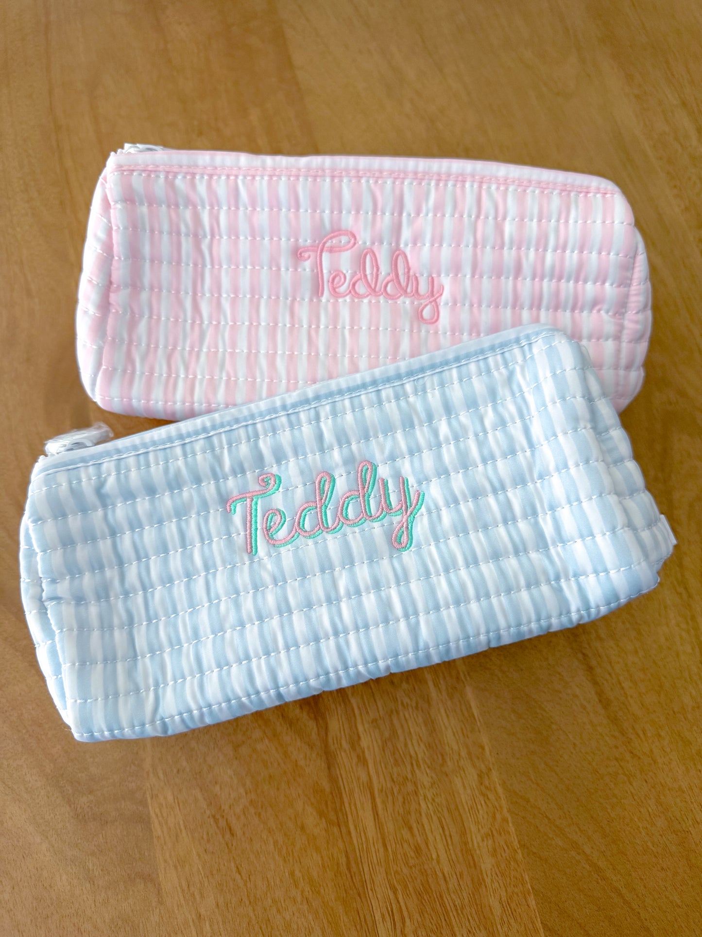 Two pouches with 'Teddy' embroidery on a wooden surface